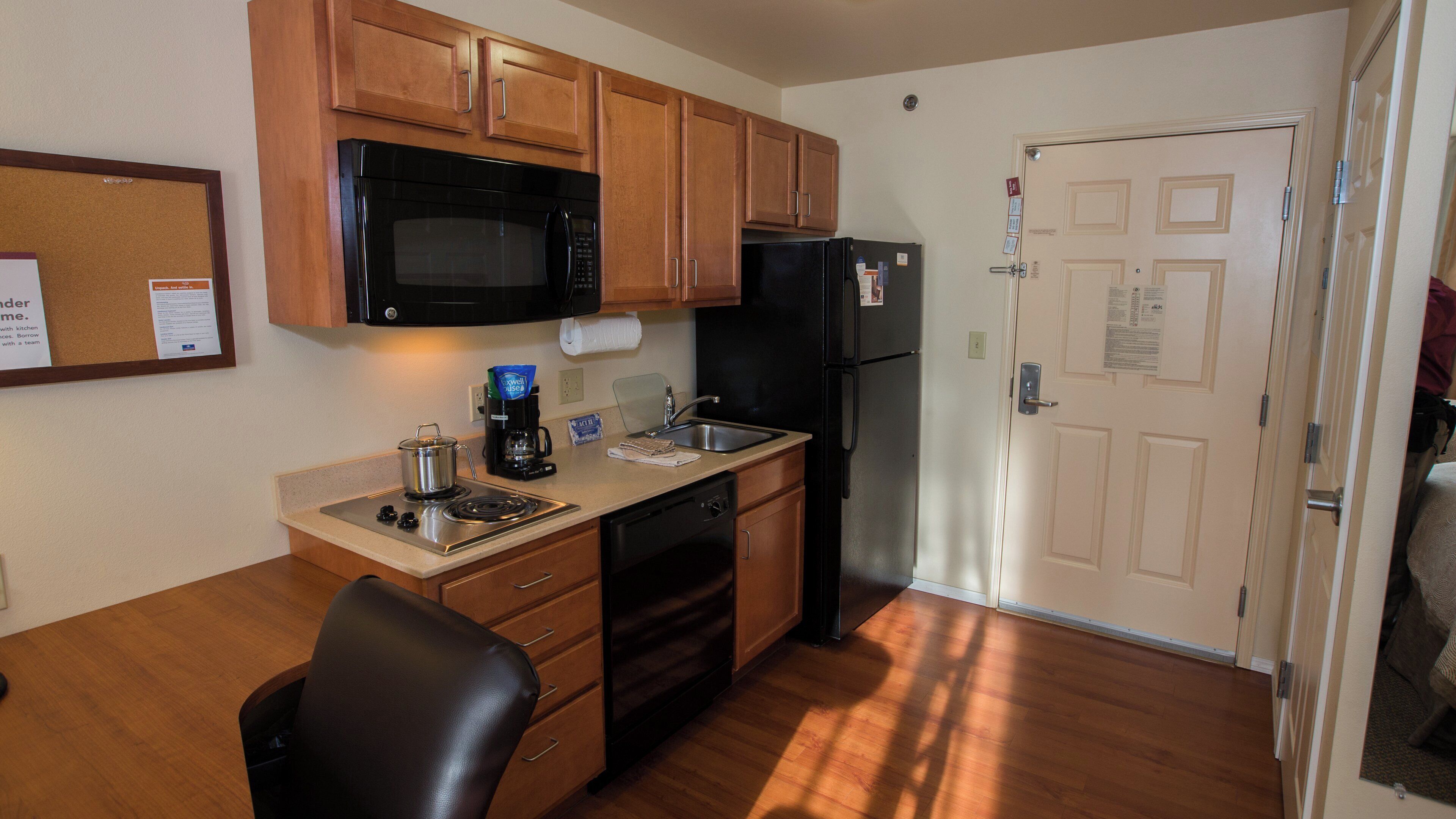 A compact kitchen with wooden cabinets, a black microwave, a refrigerator, and a coffee maker.