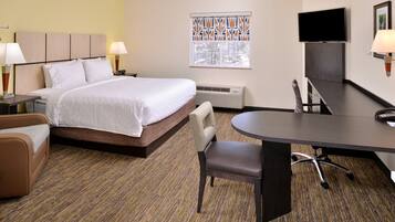 A hotel room with a bed, bedside tables with lamps, a desk with a chair, a TV mounted on the wall, and a window with a view of trees.