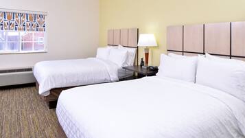 Habitación de hotel con dos camas, ventana con vista decorativa, mesita de noche con lámpara y calefactor.
