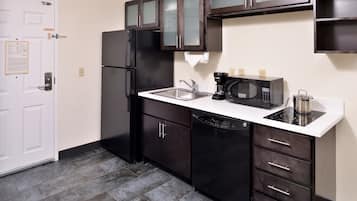 Cocina compacta con armarios oscuros, encimera blanca, refrigerador negro, cafetera y microondas.