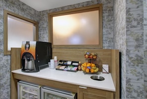A kitchenette with a coffee machine, a fruit basket, and a mini-fridge.