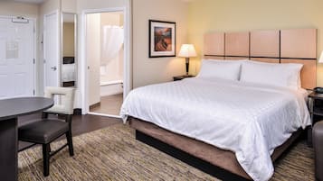 Una habitación de hotel con cama, escritorio, silla, mesita de noche y lámpara de pared.
