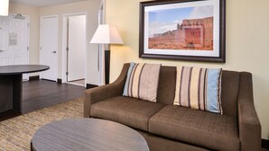 Habitación de hotel con sofá marrón, una mesita redonda, un cuadro enmarcado en la pared y una lámpara.