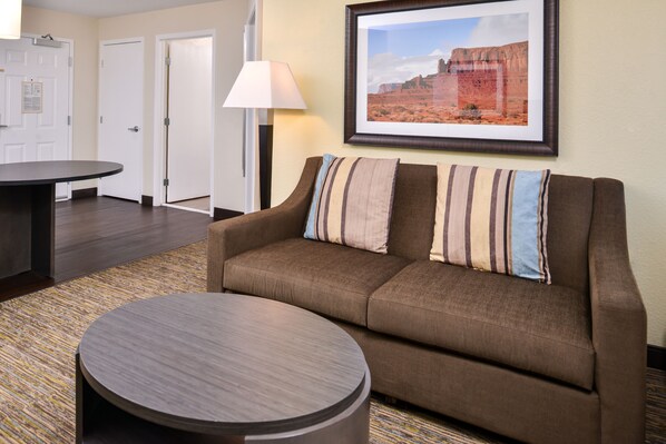 A hotel room with a brown sofa, a round coffee table, a framed picture on the wall, and a lamp. - Candlewood Suites Sierra Vista by IHG (Sierra Vista)