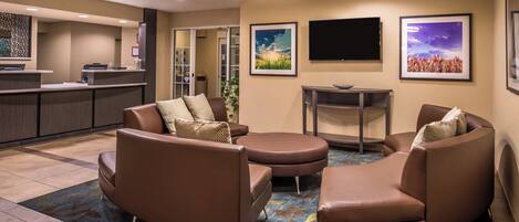 Un hall de hotel con mostrador de recepción, zona de estar con sofás y una mesa de centro, televisor de pantalla plana y obras de arte enmarcadas en las paredes.