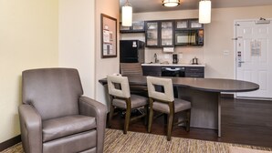 A modern hotel room with a dining area featuring a brown leather chair and a small table, a kitchen with dark cabinets and a microwave, and a wooden floor. - Candlewood Suites Sierra Vista by IHG (Sierra Vista)