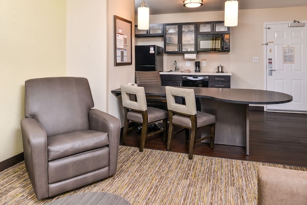 A modern hotel room with a dining area featuring a brown leather chair and a small table, a kitchen with dark cabinets and a microwave, and a wooden floor. - Candlewood Suites Sierra Vista by IHG (Sierra Vista)