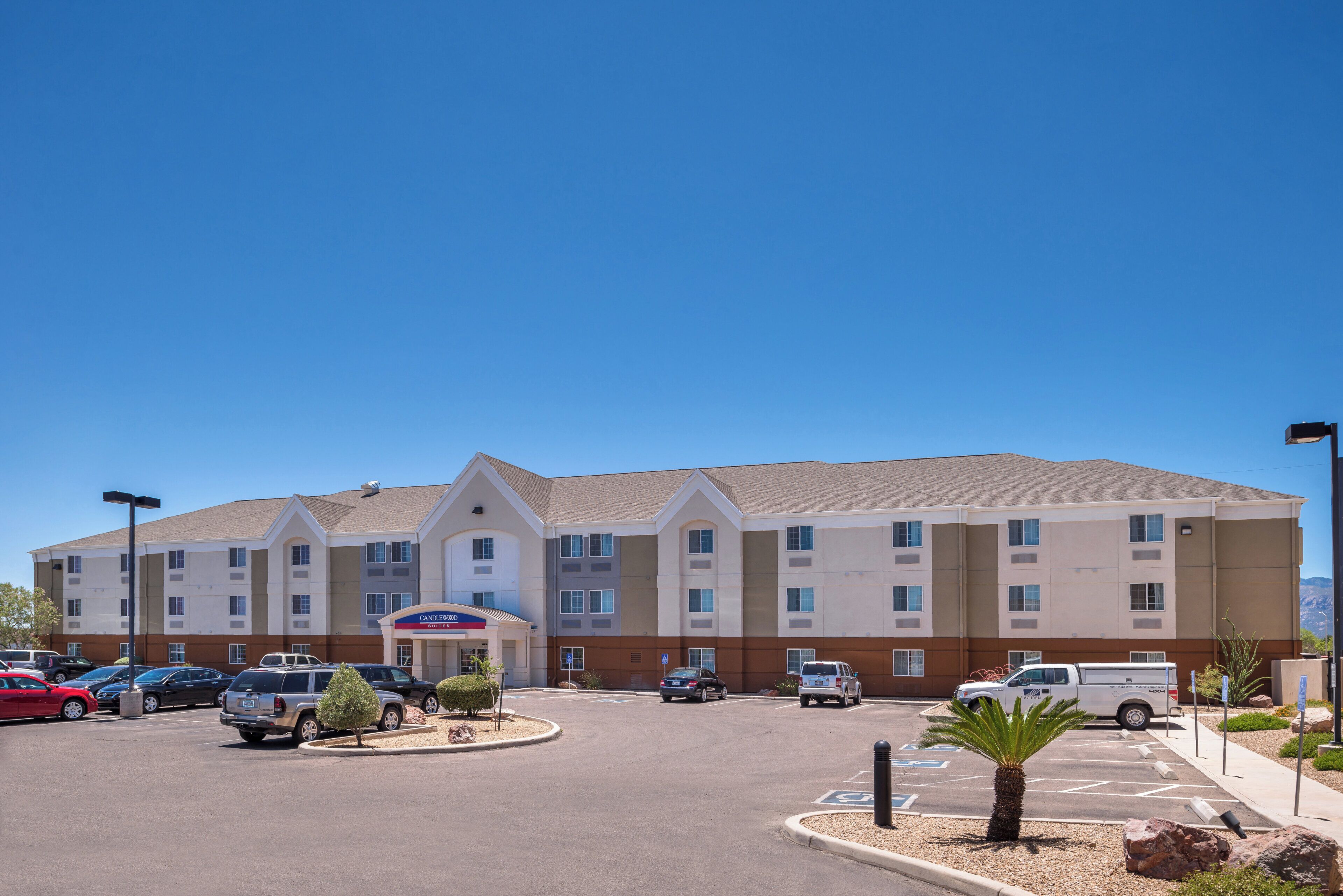 A hotel with a central entrance, multiple parking spaces, and a clear sky.