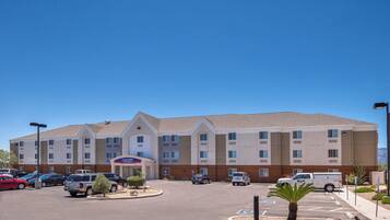 A hotel with a central entrance, multiple parking spaces, and a clear sky.