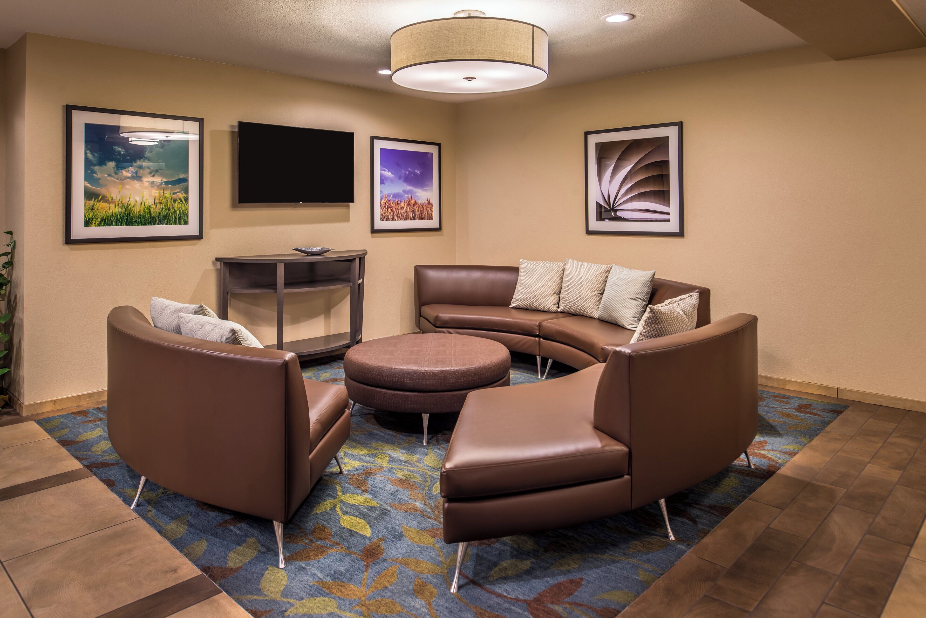 A modern living room with a brown leather sofa, a coffee table, and a flat-screen TV mounted on the wall.
