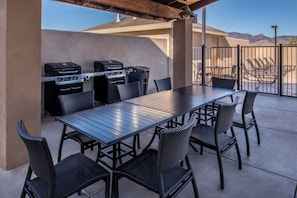 An outdoor patio with a long table and six chairs, a barbecue grill, and a trash can.