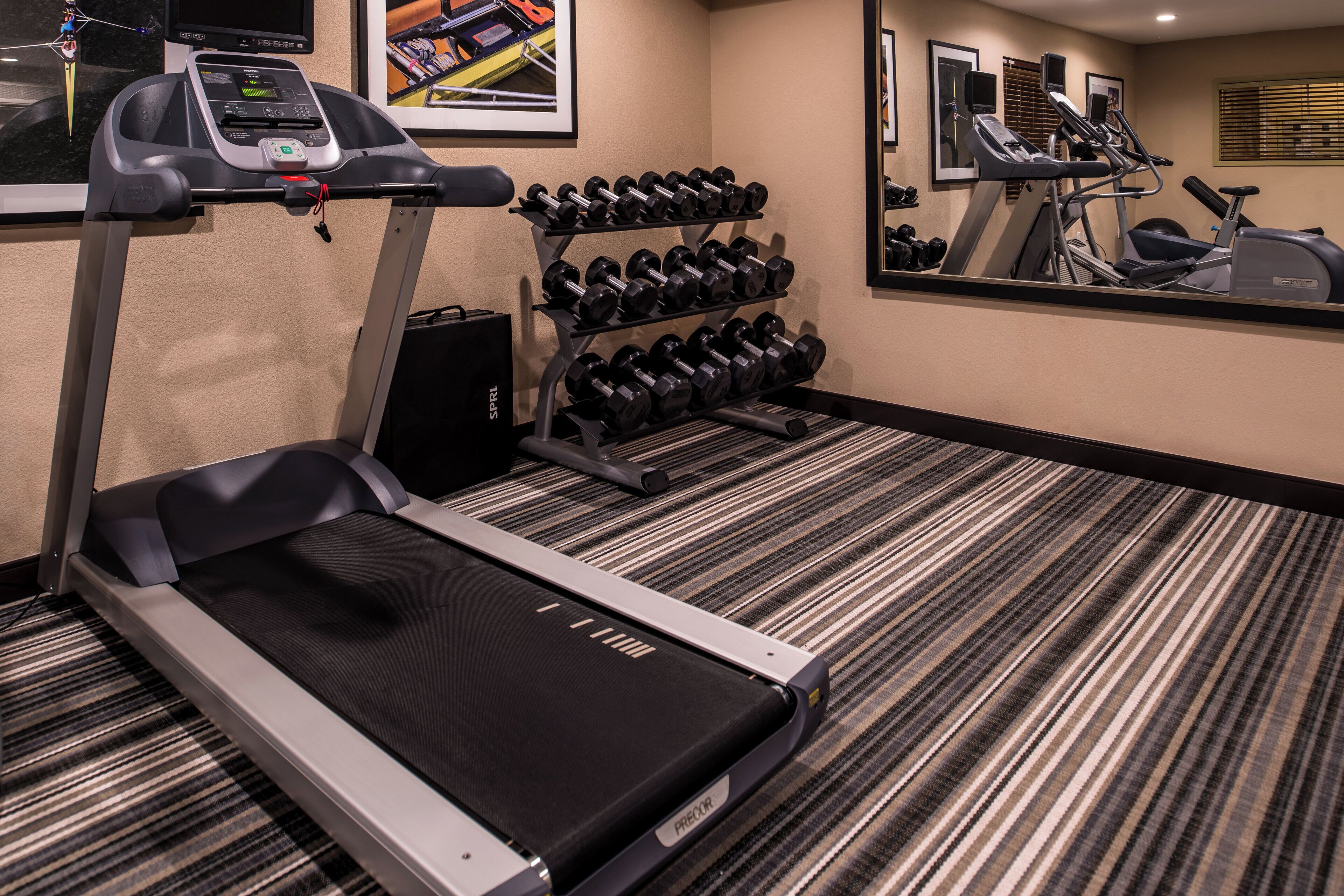 Un gimnasio hotelero con cinta de correr, un estante de mancuernas y un muro con espejos.