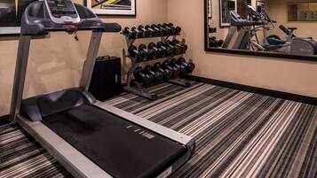 Un gimnasio hotelero con cinta de correr, un estante de mancuernas y un muro con espejos.