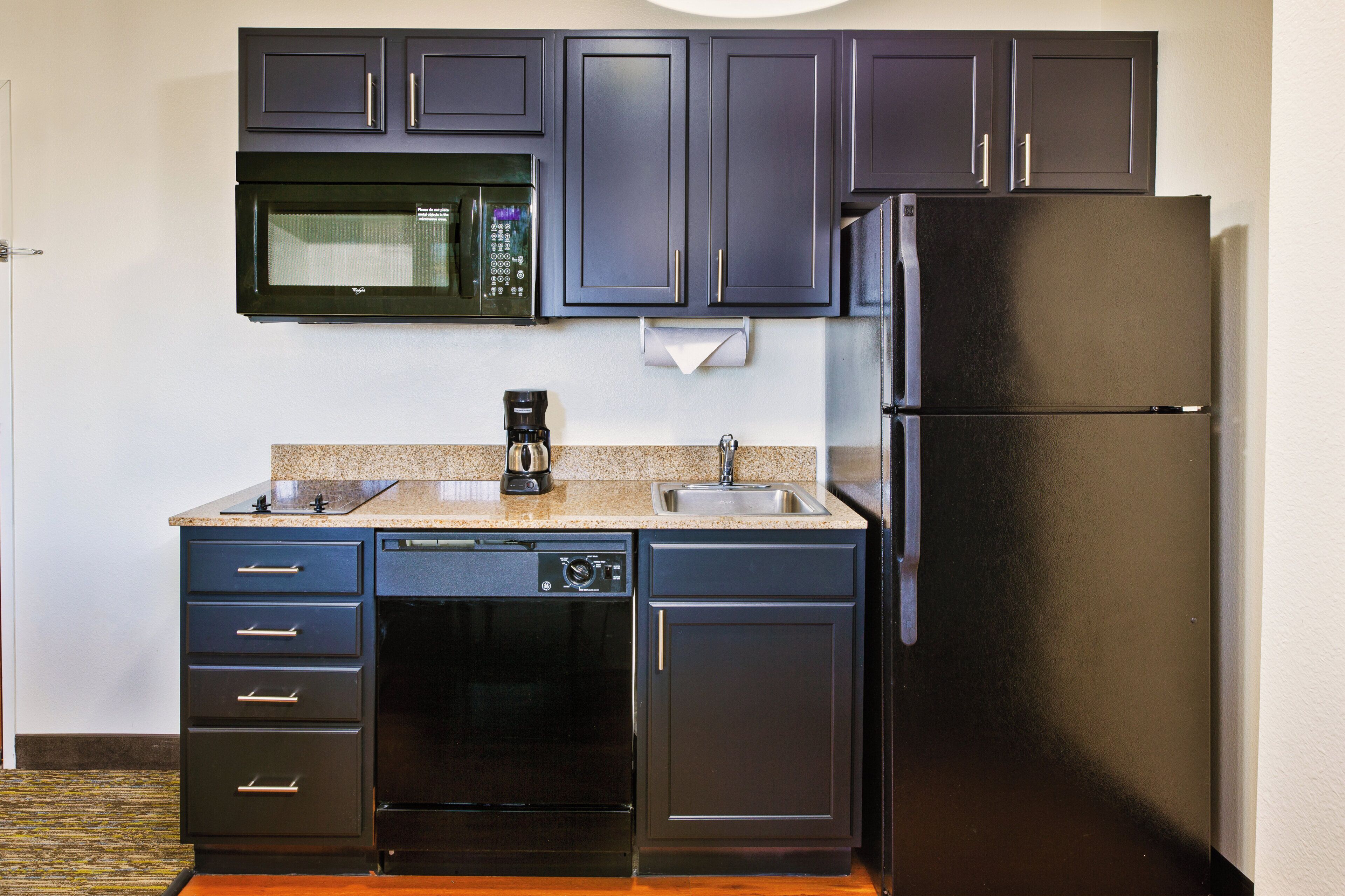 Una cocina compacta equipada con microondas, cafetera, lavavajillas y refrigerador.