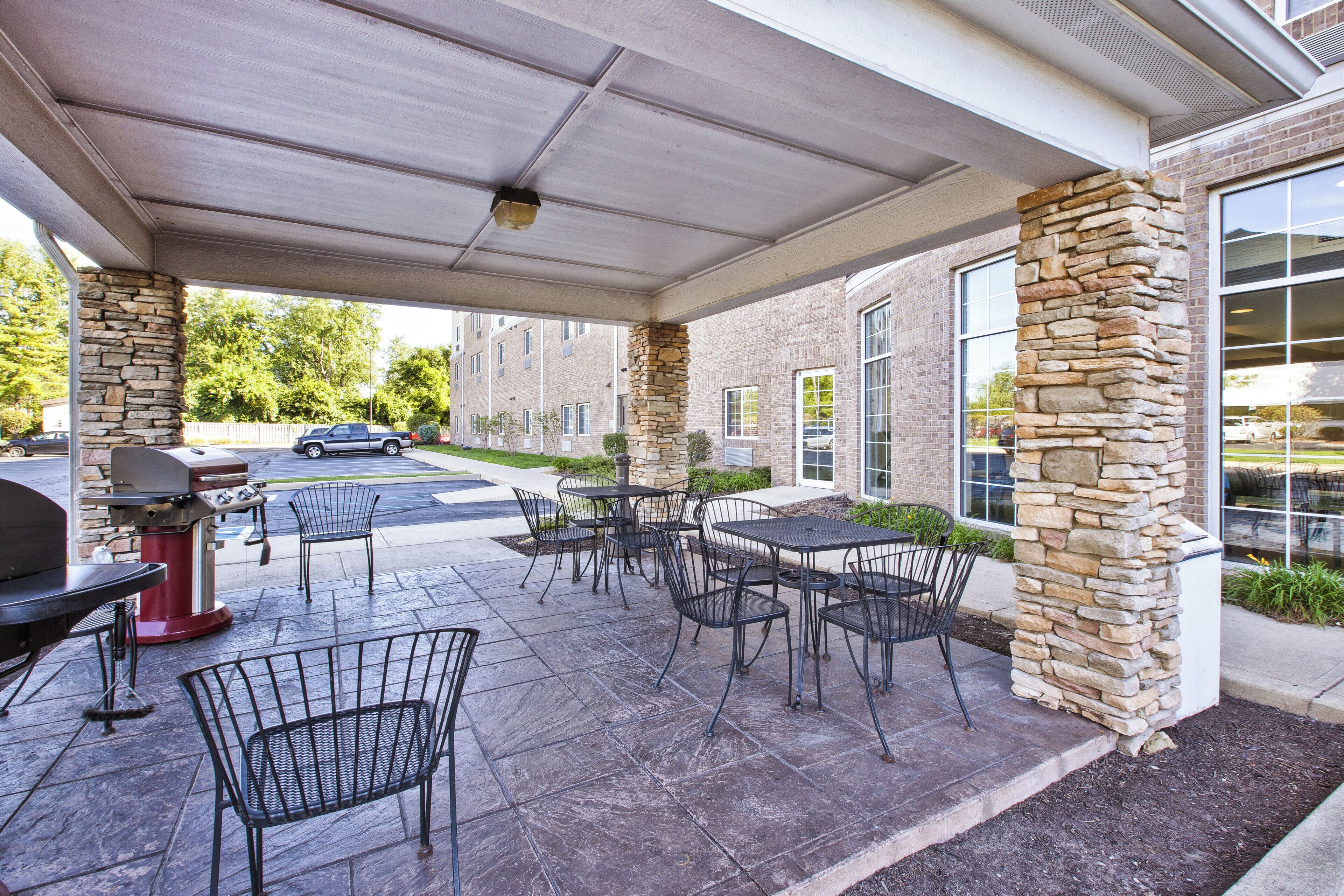 Un patio exterior con pilares de piedra, sillas de metal y una parrilla.