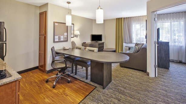 A hotel room with a conference table, chairs, a television, a sofa, and a large window with curtains.