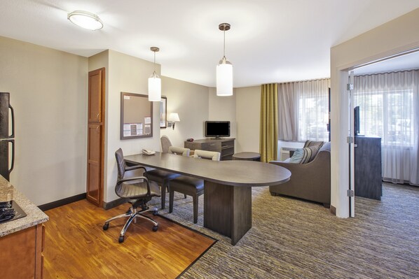 A hotel room with a conference table, chairs, a television, a sofa, and a large window with curtains. - Candlewood Suites Indianapolis Airport by IHG (Indianapolis)