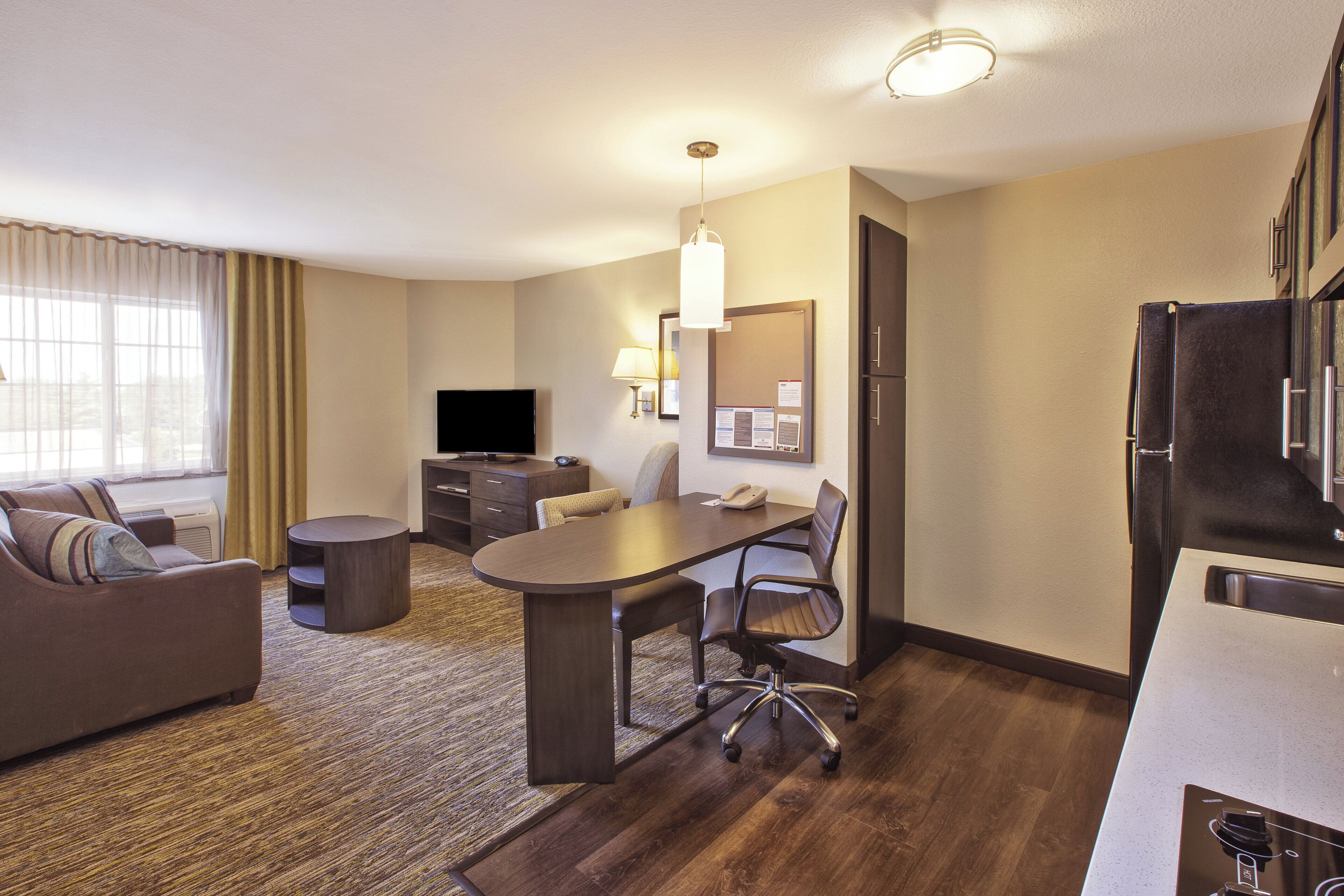 A hotel room with a living area, a dining table, a TV, a refrigerator, and a small kitchenette.