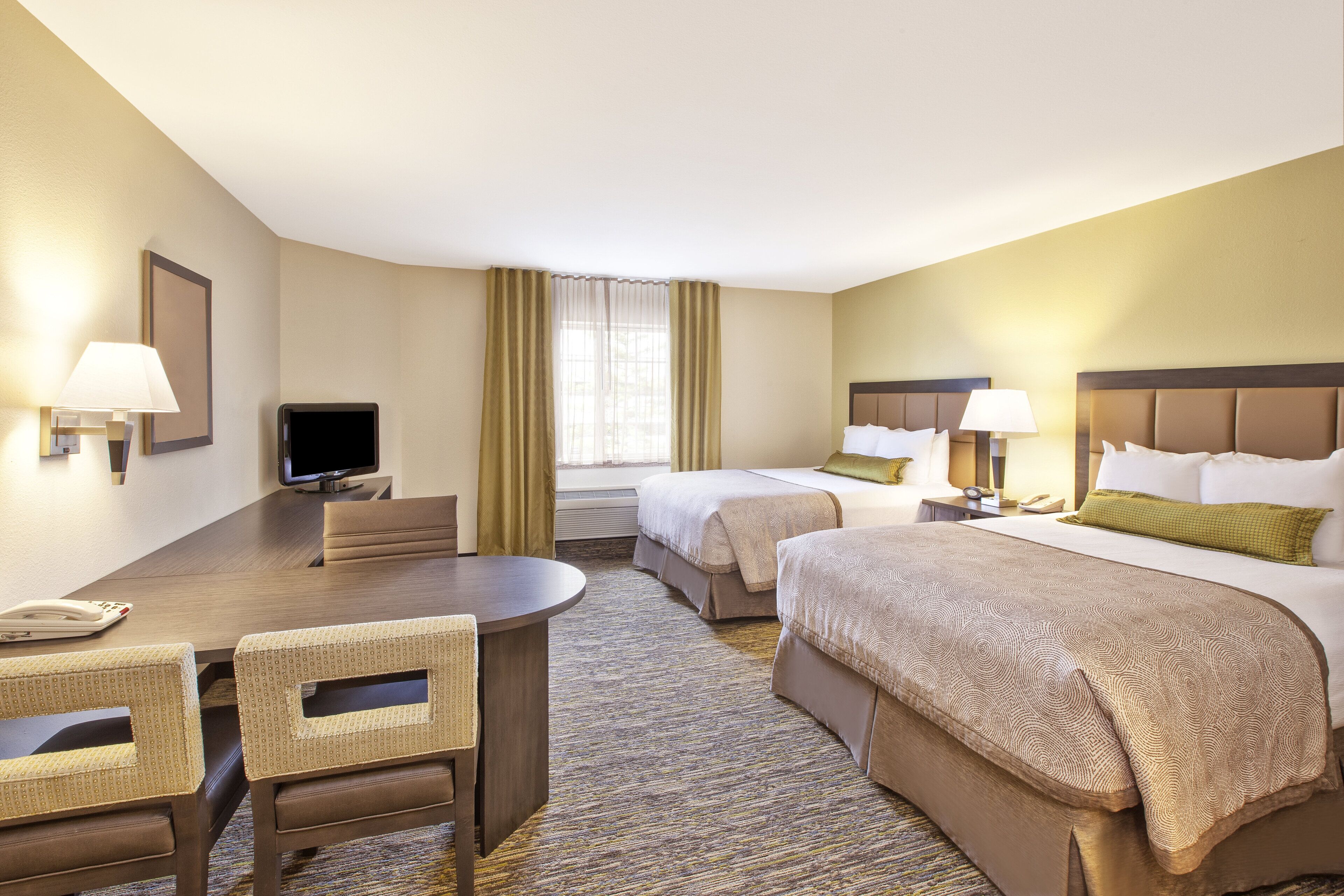 A hotel room with a desk, two beds, a TV, and a window with curtains.