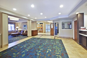 Un hall de hotel con una zona alfombrada, una recepción y un área de estar con sofá.