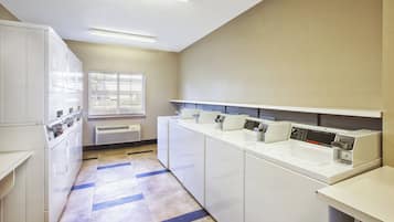 A laundry facility with multiple washing machines and dryers, a window with blinds, and a tiled floor.