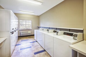 A laundry facility with multiple washing machines and dryers, a window with blinds, and a tiled floor. - Candlewood Suites Indianapolis Airport by IHG (Indianapolis)