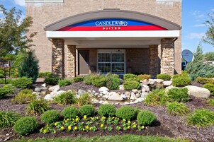 A hotel entrance with a stone facade, a landscaped garden with a water feature, and a clear sky.