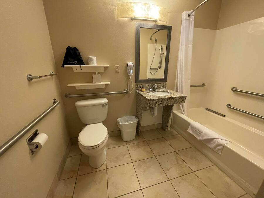 A bathroom with a toilet, sink, and bathtub, equipped with grab bars and a shower.