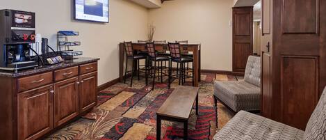 Une chambre d’hôtel équipée d’un coin café, d’un espace repas avec des chaises et une table, et d’un tapis à motifs.