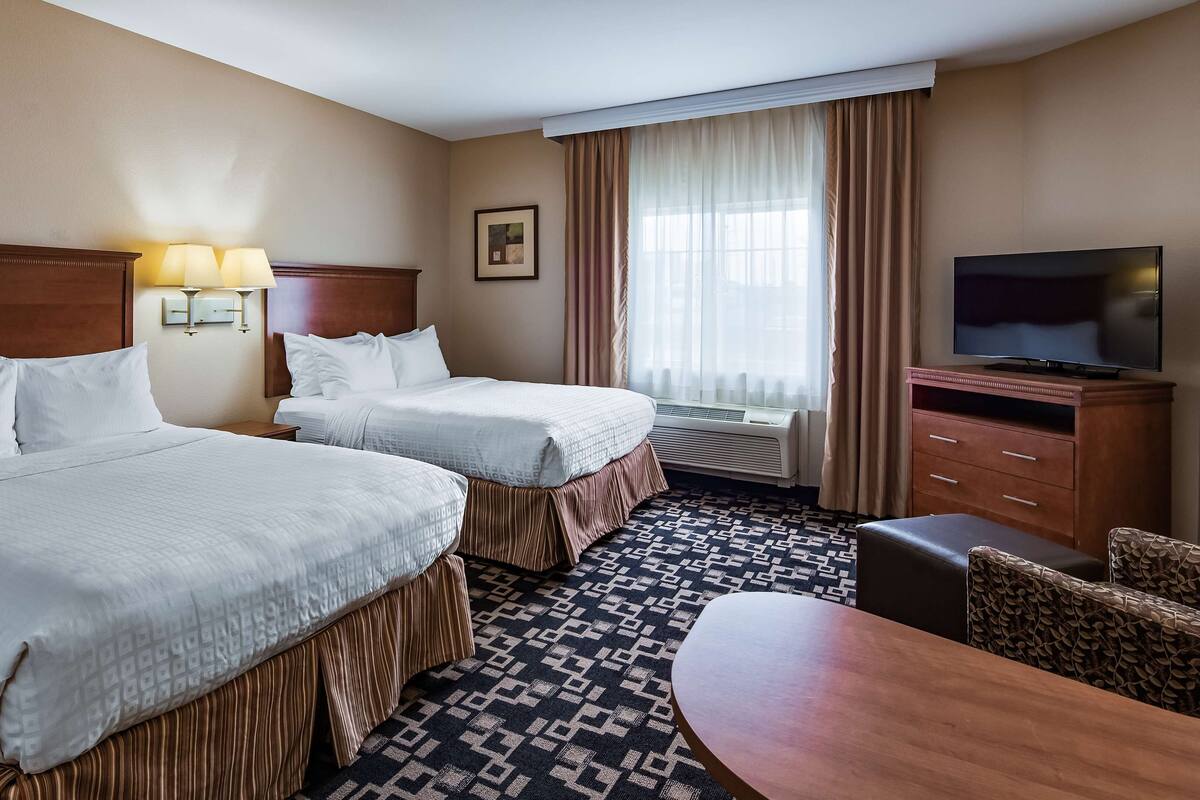 A hotel room with two beds, a TV, a desk, and a chair.