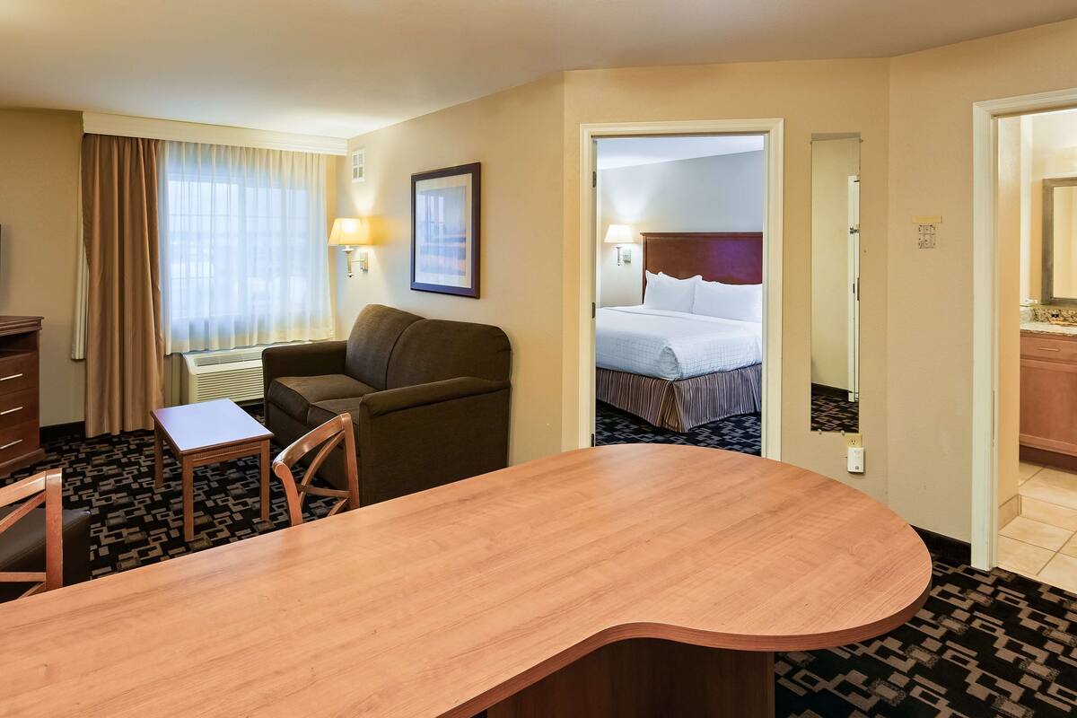 A hotel room with a wooden desk, a sofa, a television, a bed, and a bathroom visible through an open door.