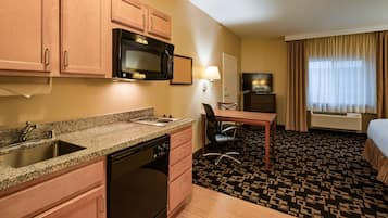A hotel room with a kitchenette, a dining area, a TV, and a bed.