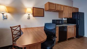 A compact kitchen with wooden cabinets, a black refrigerator, a microwave, and a dining table with chairs.