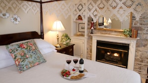 Un dormitorio con cama, chimenea y una bandeja con aperitivos y vino.