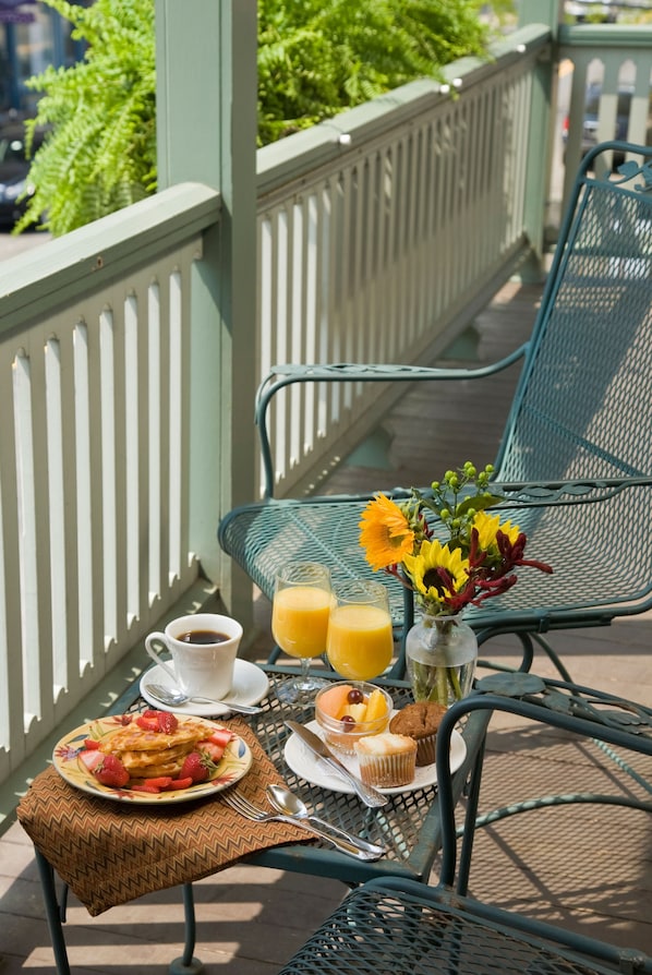 A breakfast setup on a balcony with a wicker table, a metal chair, a white fence, and greenery in the background. - Lambertville House (Lambertville)