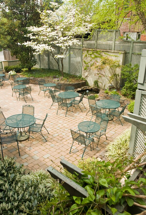 An outdoor patio area with round tables and chairs, surrounded by a brick wall and greenery.