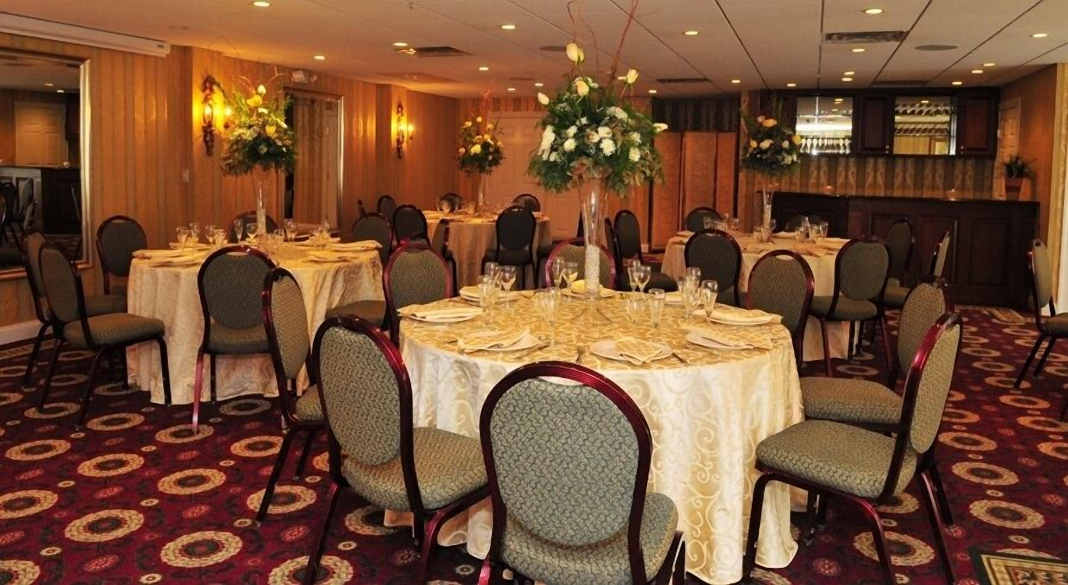 Salão de banquetes com mesas redondas dispostas para refeições, cada uma com cadeiras e centros de mesa.