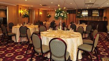 Salão de banquetes com mesas redondas dispostas para refeições, cada uma com cadeiras e centros de mesa.