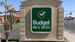 A Budget Inn & Suites sign with a green background and white text, surrounded by a stone wall and a small lawn. - Budget Inn and Suites El Centro (El Centro)