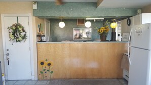 A kitchen with a wooden counter, a refrigerator, a wall-mounted clock, and a hanging light fixture. - Budget Inn and Suites El Centro (El Centro)