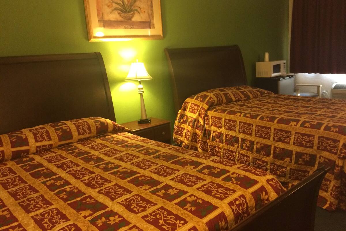 Hotellihuone, jossa on kaksi sänkyä, yöpöytä lampun kanssa, mikroaaltouuni ja taulu seinällä.