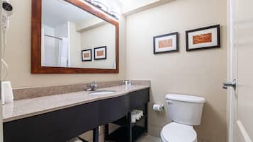 Ein Badezimmer mit Waschbecken, Spiegel, Toilette und einem gerahmten Kunstwerk an der Wand.