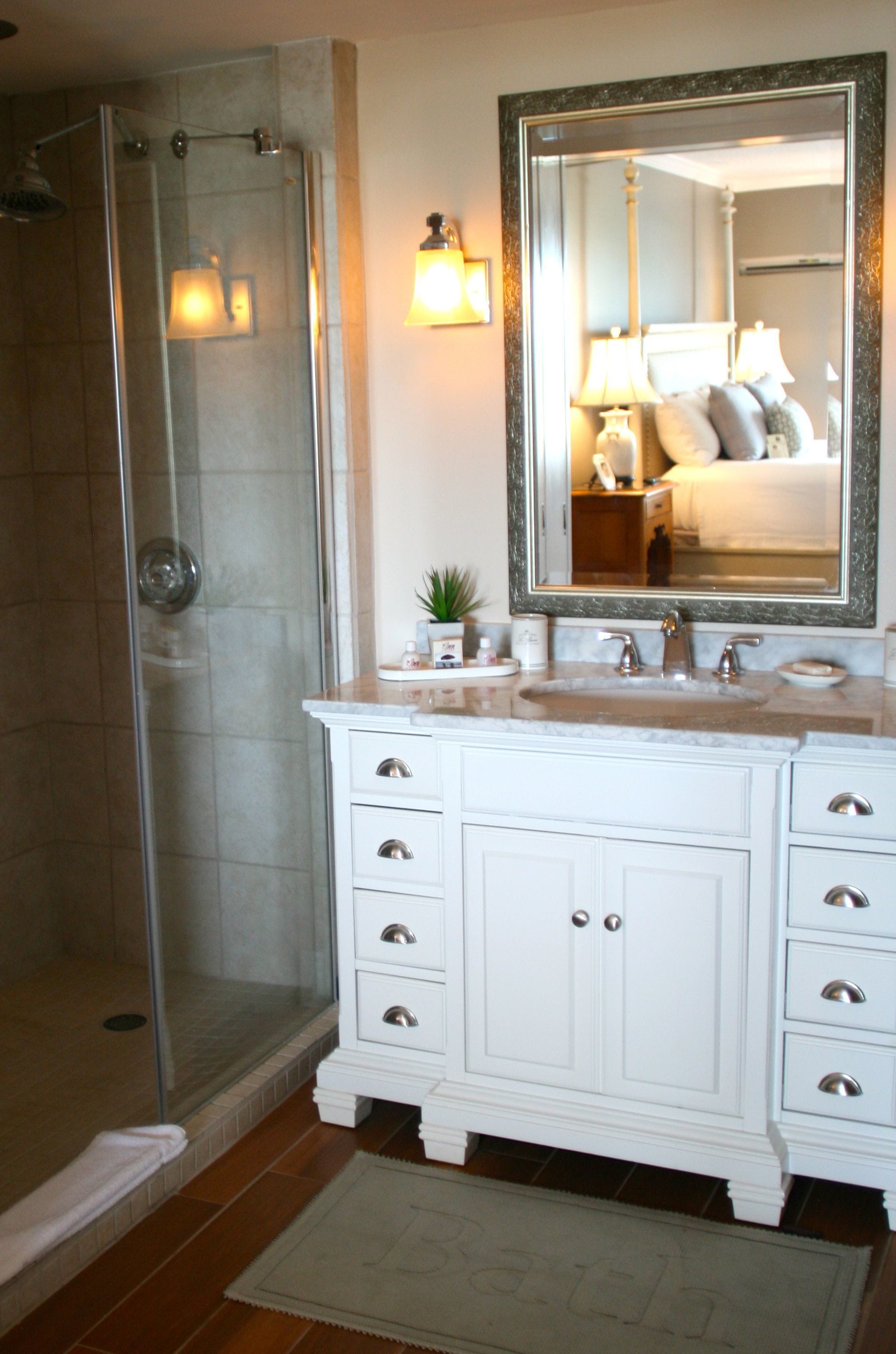 A bathroom with a glass shower enclosure, a white vanity with a sink, and a large mirror above the vanity.