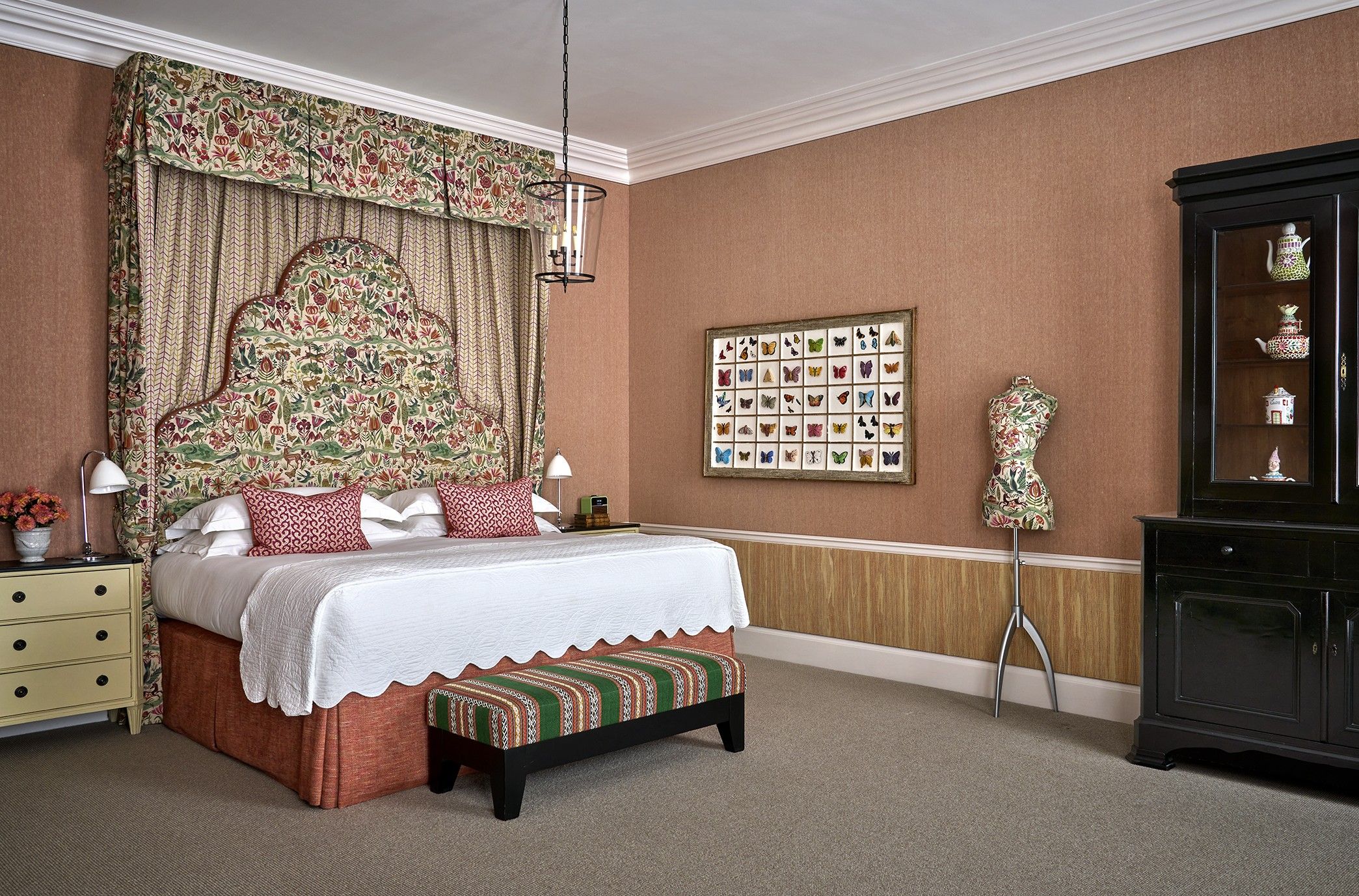 A bedroom with a large bed, a nightstand, a dresser, a wall-mounted shelf, and a framed butterfly collection.