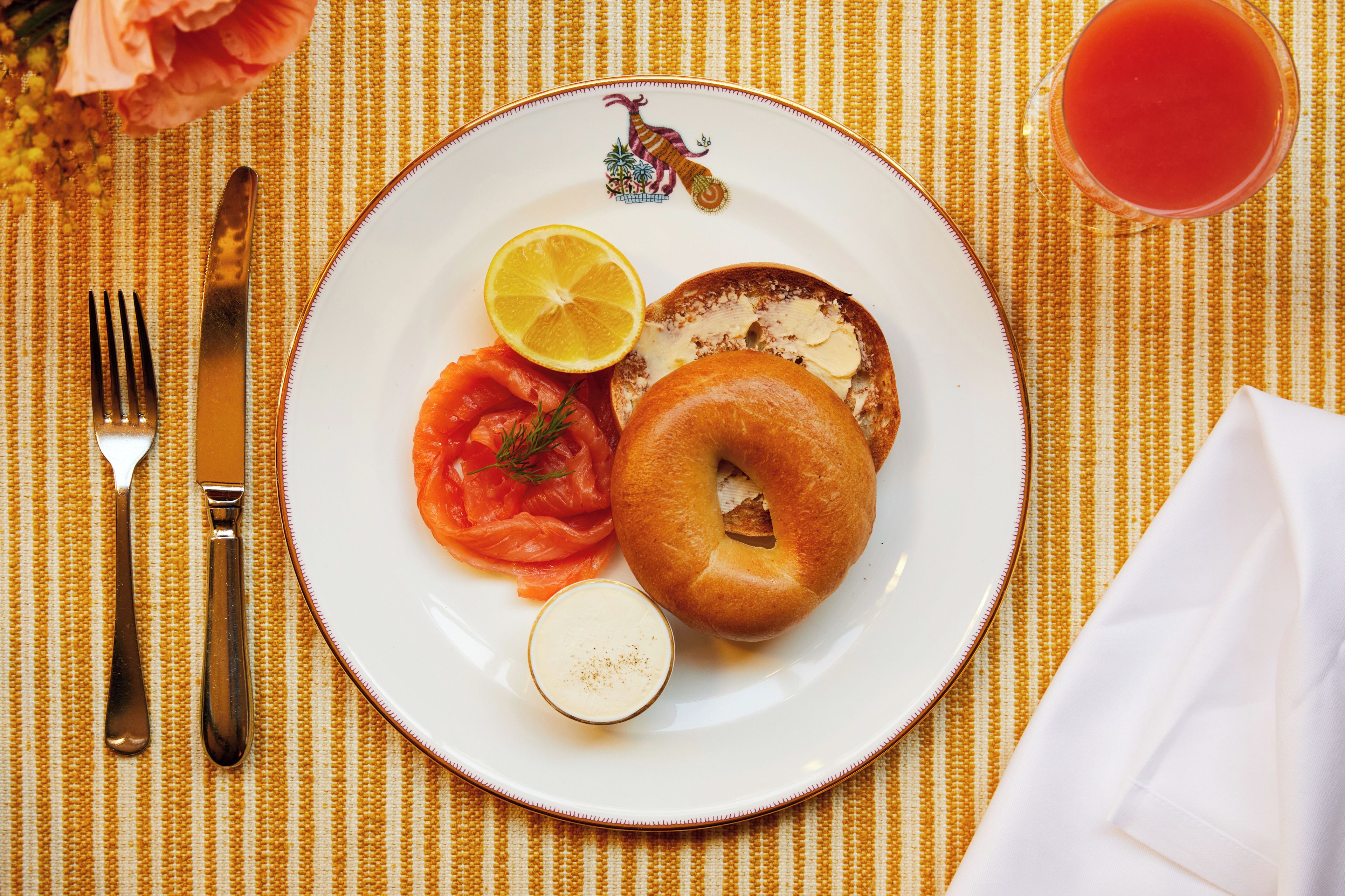 Une assiette contenant un bagel, du saumon fumé, une tranche de citron et une cuillerée de fromage frais, le tout posé sur une nappe.