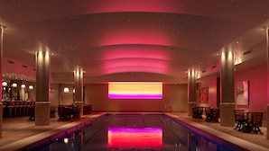 Una piscina interior espaciosa con diseño moderno, que cuenta con una zona de bar en un lado y espacios de descanso en el otro.