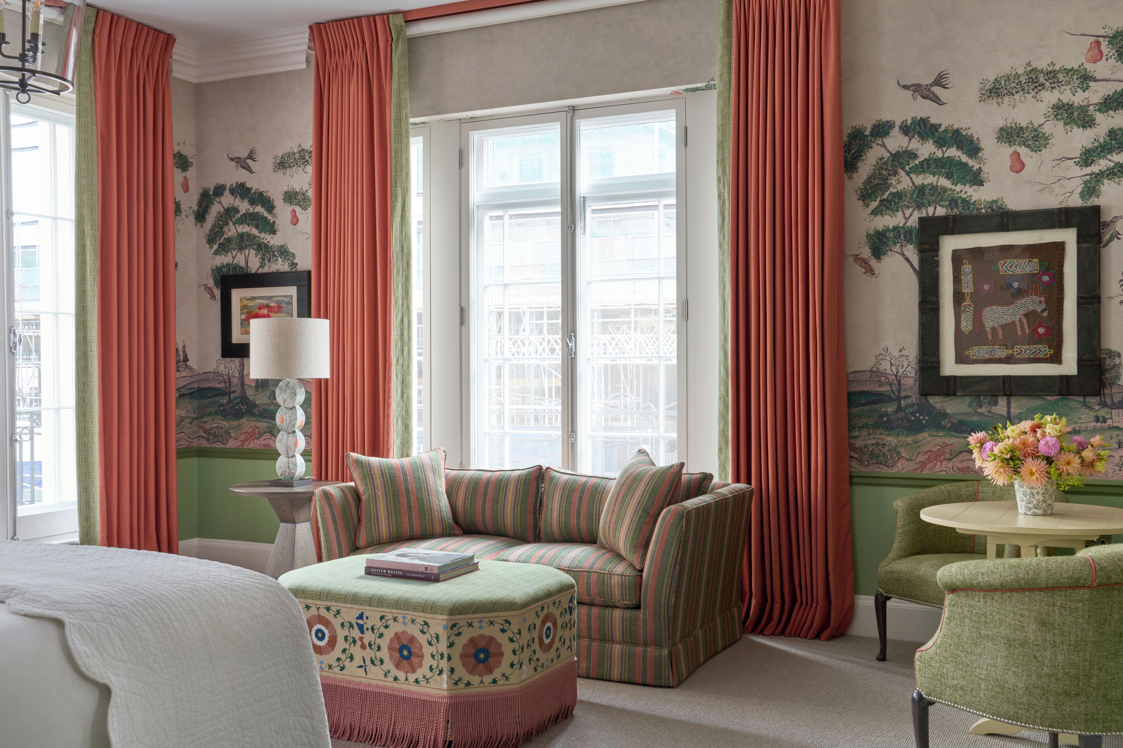 A room with a green sofa, a small table with a vase, and a window with curtains.