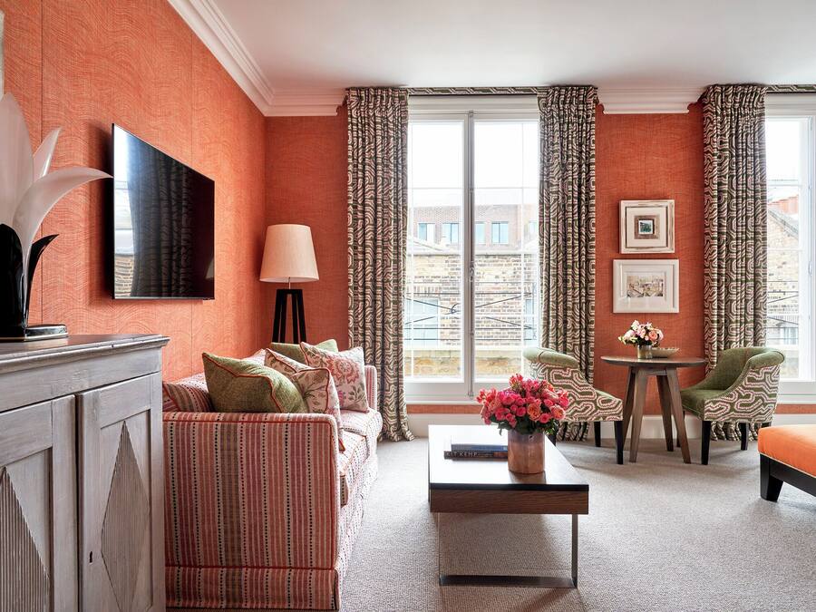 A hotel room with a sofa set, a coffee table, a lamp, a TV, and a view of the city through large windows.