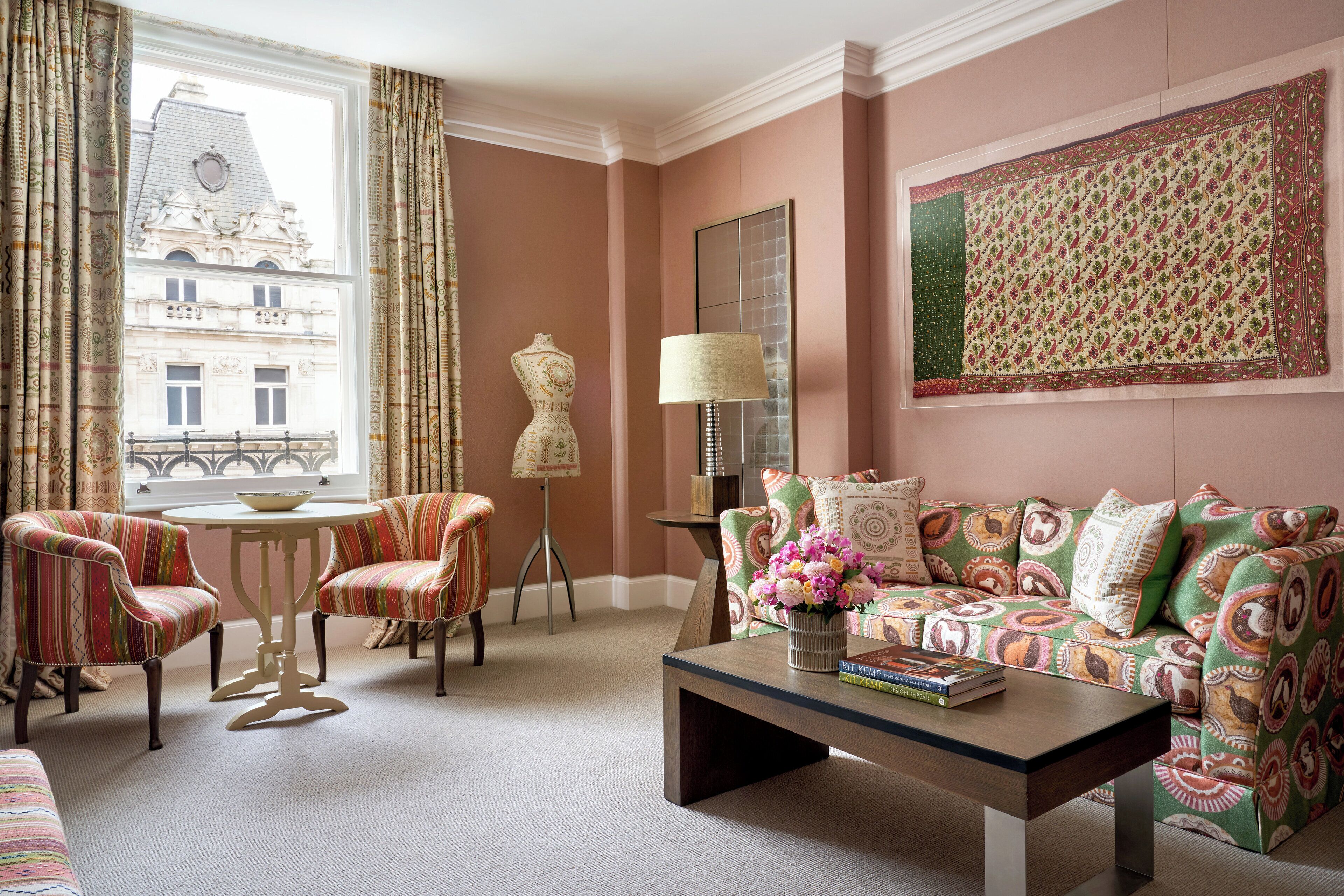 A room with a sofa, two armchairs, a coffee table, a lamp, and a view of a building through a window.