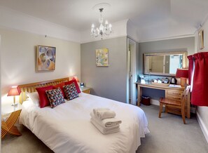 A neatly arranged bedroom with a bed, bedside table, lamp, and a desk with a mirror. - The Claremont (Hove)
